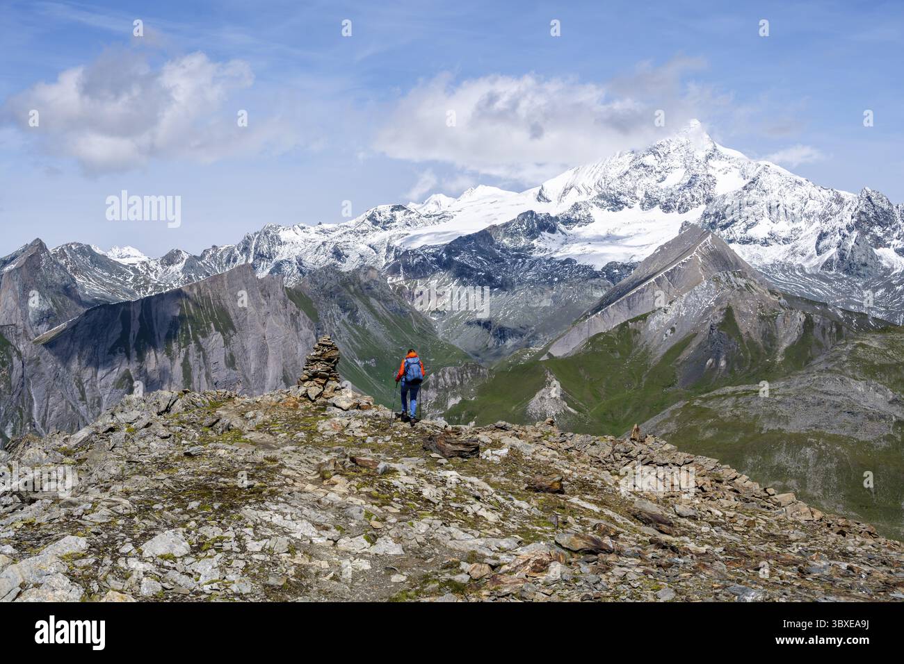 Bergsteigerin auf Wanderweg mit Kairn, hinter vergletschtem und schneebedecktem Gipfel des Großglockners, Wiener Hoehenweg, Schober-Gruppe, hohe Ta Stockfoto