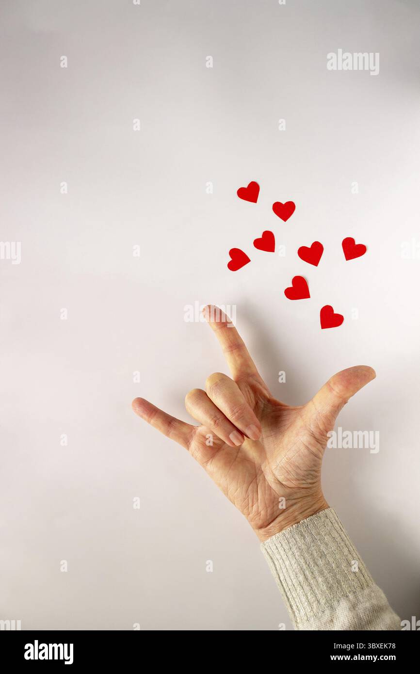 Der Satz Ich liebe dich in Gebärdensprache, die Sprache der Tauben. Frauenhand auf weißem Hintergrund mit roten Papierherzen, Kopierraum Stockfoto