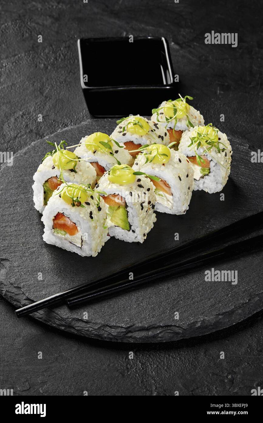 Frisch zubereitete Uamaki-Sushi-Brötchen werden auf einem schwarzen Schieferteller mit Lachs, Avocado und Frischkäse serviert, garniert mit Mikrogrün, SE Stockfoto