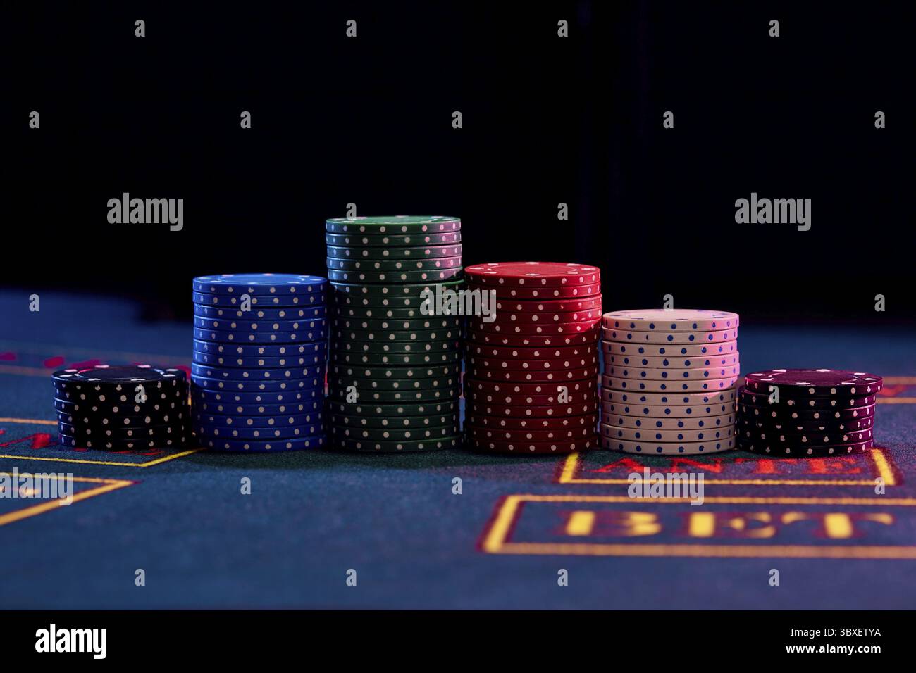 Bunte chips Pfählen stehend auf einem blauen Abdeckung der Tabelle mit Markup, vor einem schwarzen Hintergrund. Spielende Unterhaltung, Poker, Casino co Stockfoto