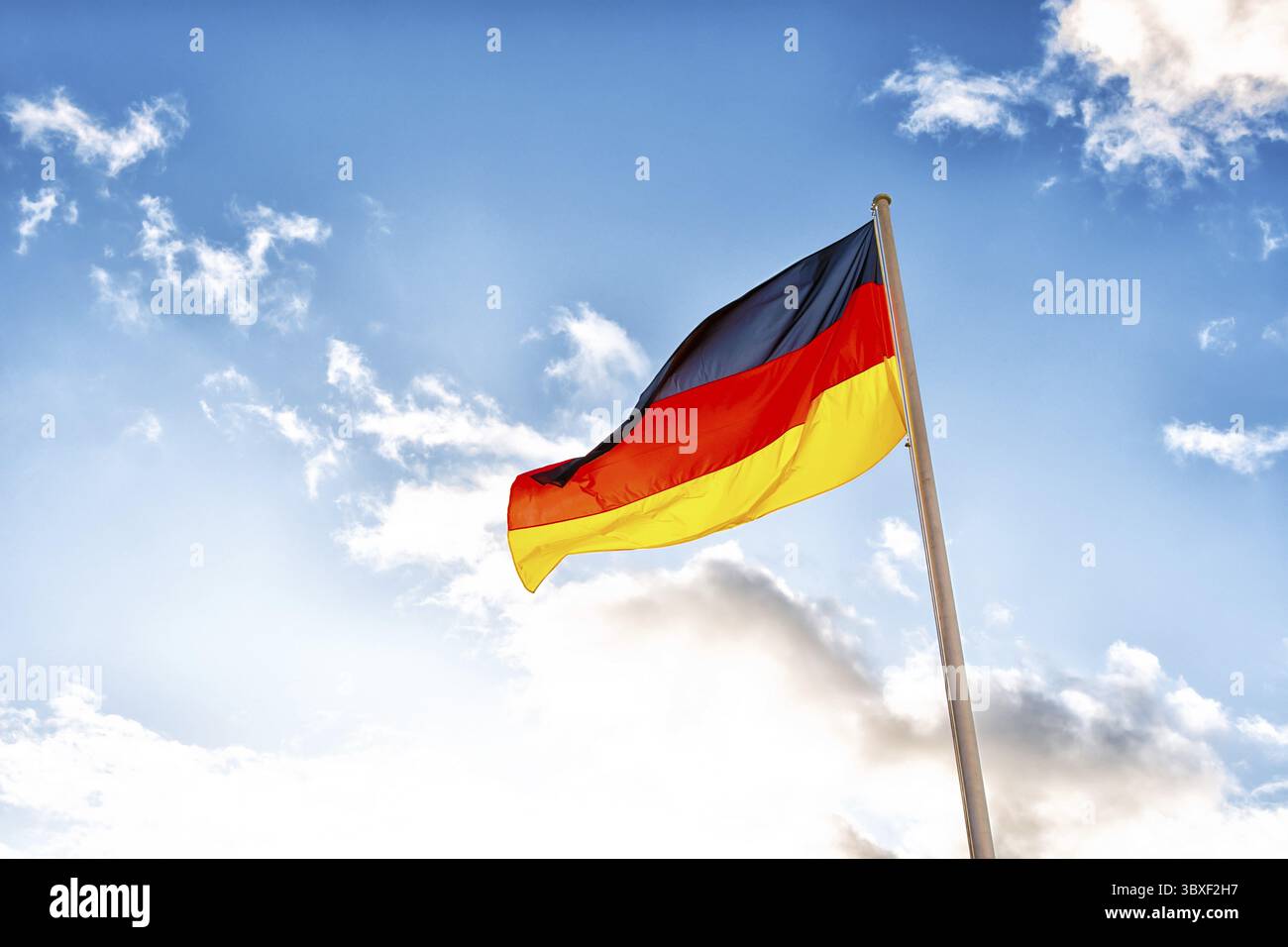Eine deutsche Flagge mit schwarzen, roten und gelben Streifen vor Wolken in blauem Himmel Stockfoto