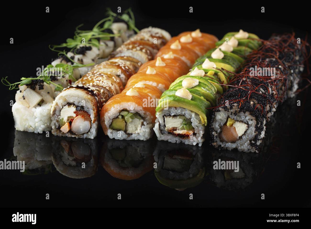 Traditionelle, köstliche, frische Sushi-Rolle auf schwarzem Hintergrund mit Spiegelung. Sushi-Rolle mit Reis, Nori, Frischkäse, Tobiko-Kaviar, Avocado. So Stockfoto