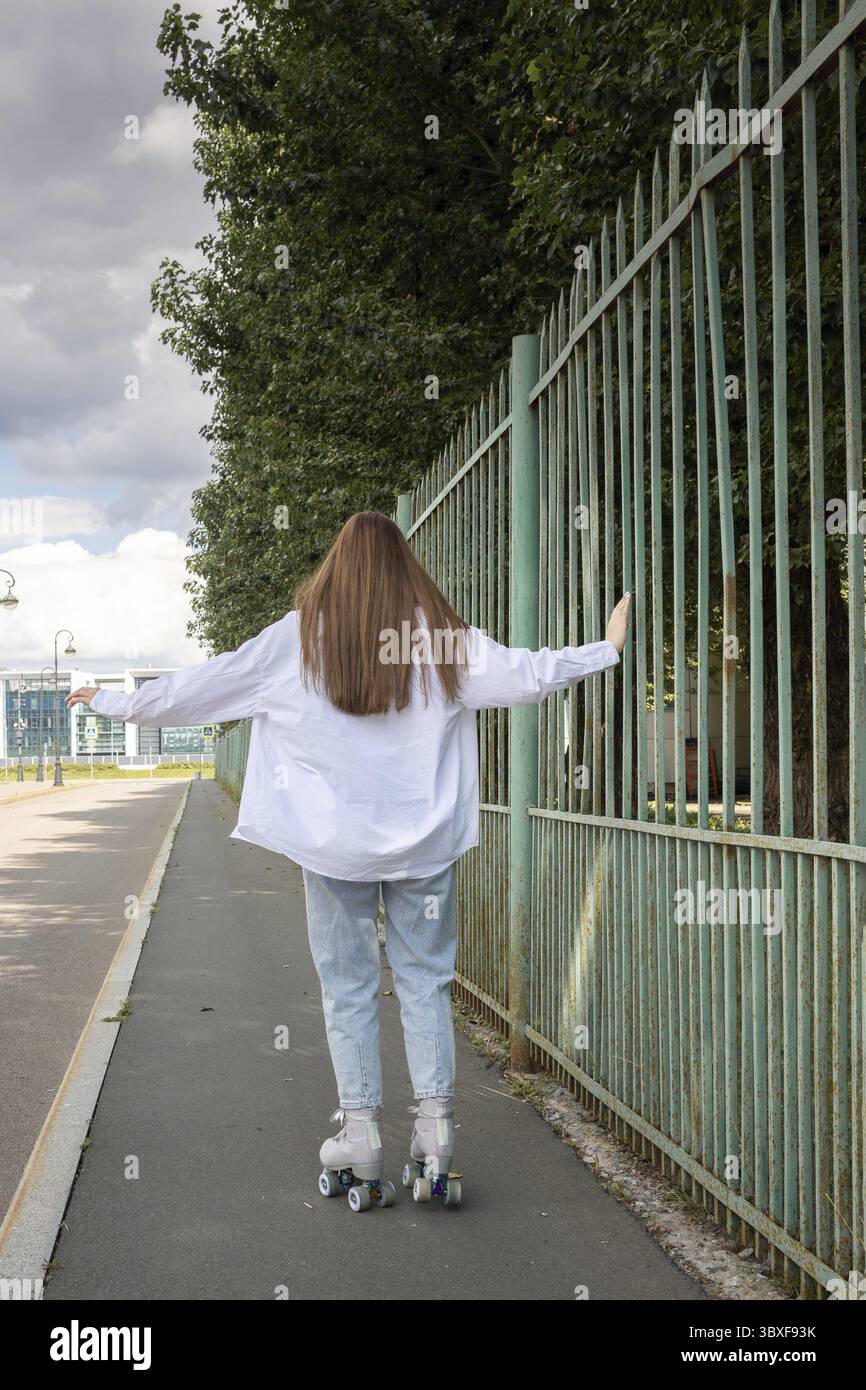Wunderschönes Mädchen mit langen Haaren, das im Park herumläuft. Rollschuhlaufen Quad - beliebte und sichere Art der Erholung. Vertikales Foto. Stockfoto