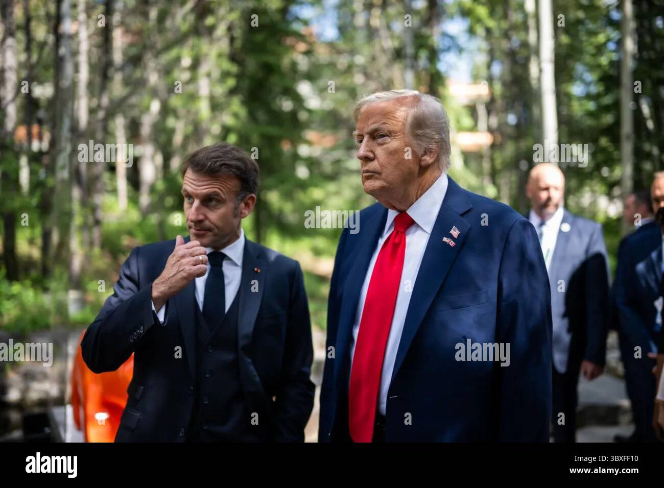 Kananaskis, Alberta, Kanada. Juni 2025. Präsident Donald J. Trump geht mit dem französischen Präsidenten Emmanuel Macron während der G7-Gipfelgespräche. Die Staats- und Regierungschefs führten Gespräche über Spannungen im Nahen Osten, Handelsabkommen und Klimapolitik in einer waldreichen Umgebung in der Nähe des Gipfeltreffens. Stockfoto