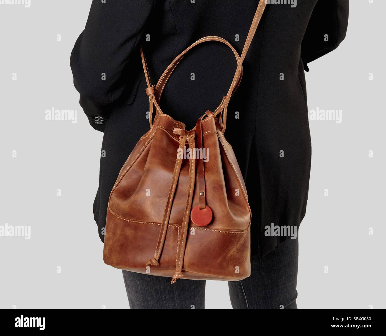 Frau in schwarzem Mantel mit schicker, brauner Ledertasche mit motivierendem Slogan über der Schulter. Stilvolle, handwerkliche Accessoires für Damen Stockfoto
