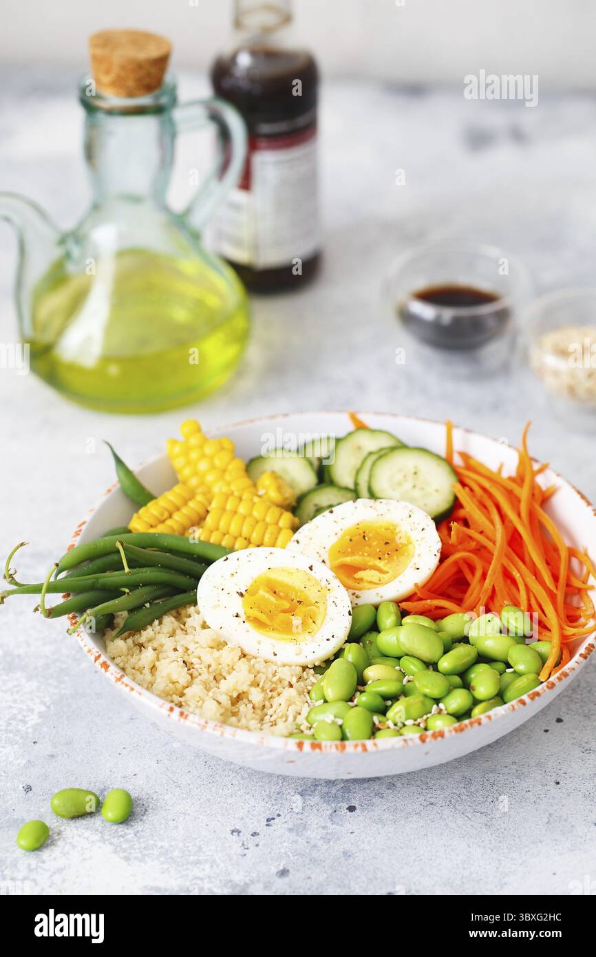Gesunder Salat mit Couscous, Karotten, Gurken, grünen Bohnen, Sojabohnen, Mais und ein Ei auf grauem Betongrund. Lebensmittel und Gesundheit. Buddha-Schale Sal Stockfoto