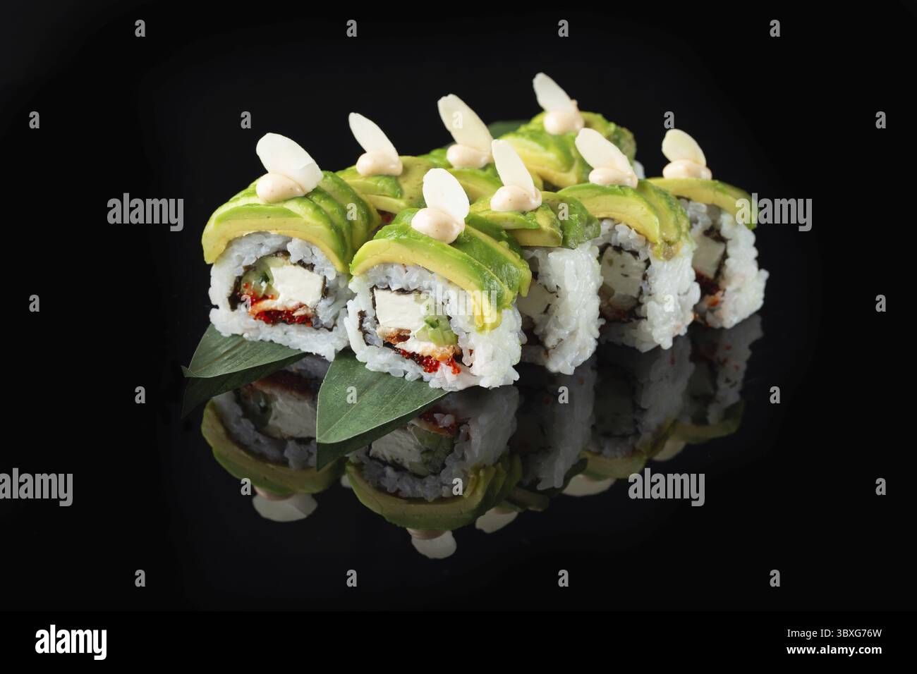 Traditionelle, köstliche, frische Sushi-Rolle auf schwarzem Hintergrund mit Spiegelung. Sushi-Rolle mit Reis, Nori, Frischkäse, Tobiko-Kaviar, Avocado. So Stockfoto