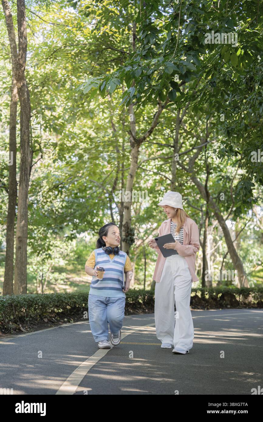 Zwei Frauen genießen einen Spaziergang durch den Park und zeigen Vielfalt und Inklusion. Eine Frau hat eine Achondroplasie, die Bewusstsein und Verständnis fördert Stockfoto