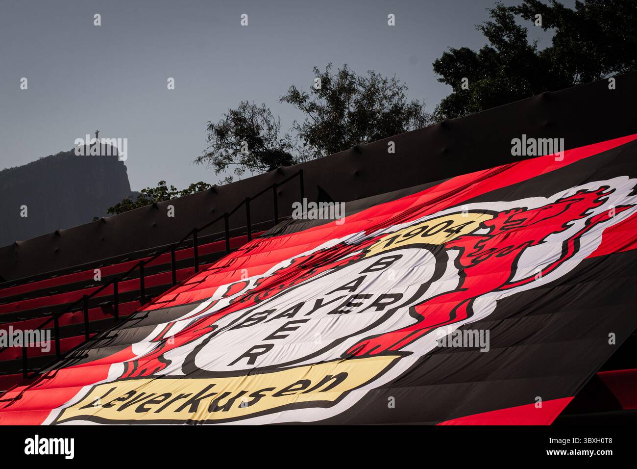 Rio De Janeiro, Brasilien. Juli 2025. Fußball: Testspiel, Flamengo U20 - Bayer Leverkusen, da Gavea Stadion. Eine riesige Flagge mit dem Bayer Leverkusen Logo hängt über den Ständen vor dem Hintergrund der Christusstatue in der brasilianischen Metropole. Quelle: Joao Gabriel Alves/dpa/Alamy Live News Stockfoto