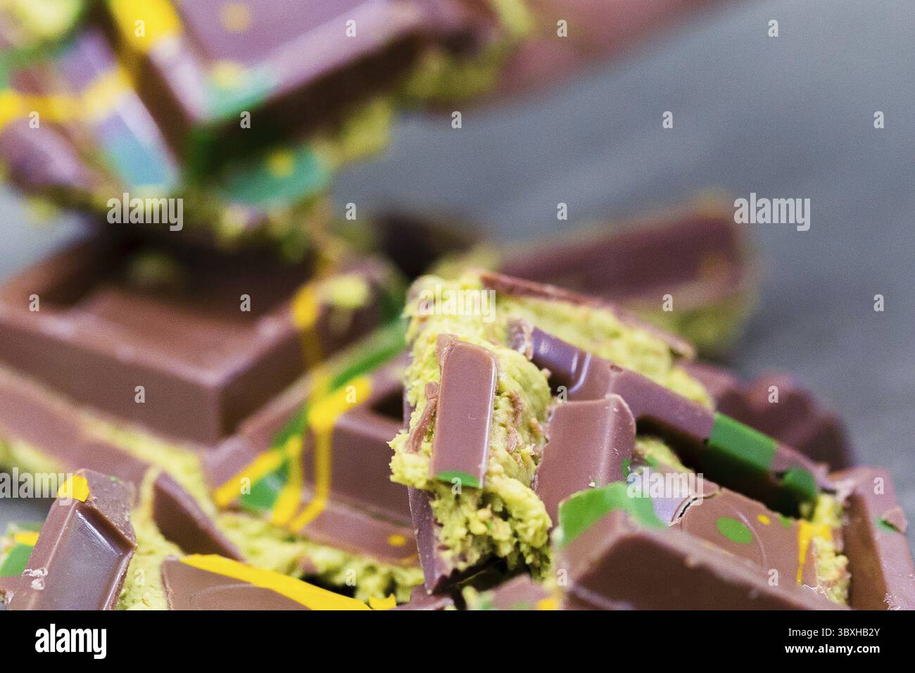 Ein Stück Dubai-Schokolade auf grauem Hintergrund. Grüner Kadayif und Pistazien mit Pistazien im Trenddessert. Nahaufnahme, selektiver Fokus. Stockfoto
