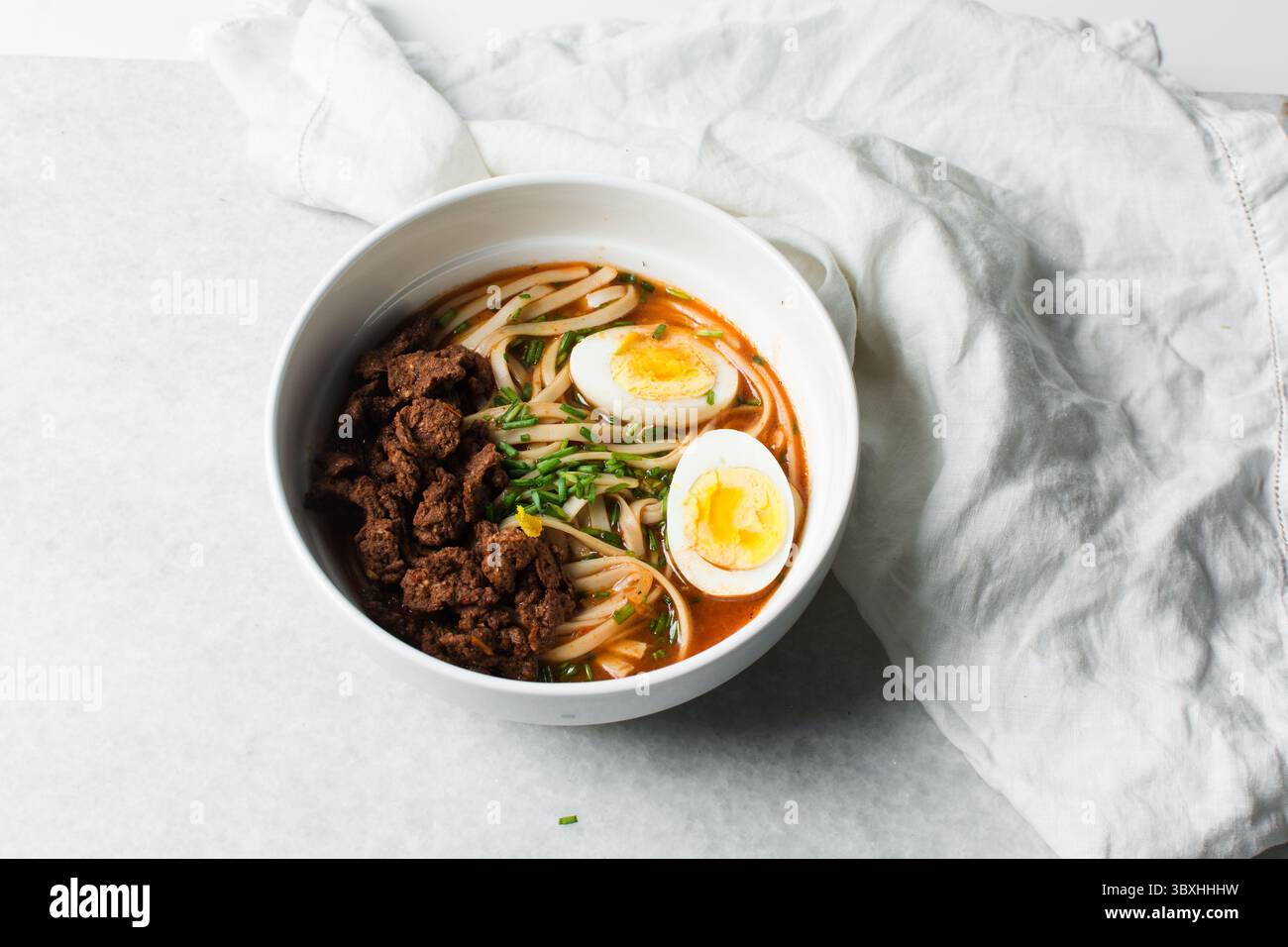 Blick von oben auf scharfe Nudelsuppe mit Eiern und Rindfleischstücken in einer weißen Schüssel, Blick von oben auf Nudeln Eier in einer scharfen Brühe mit Zwiebeln Stockfoto