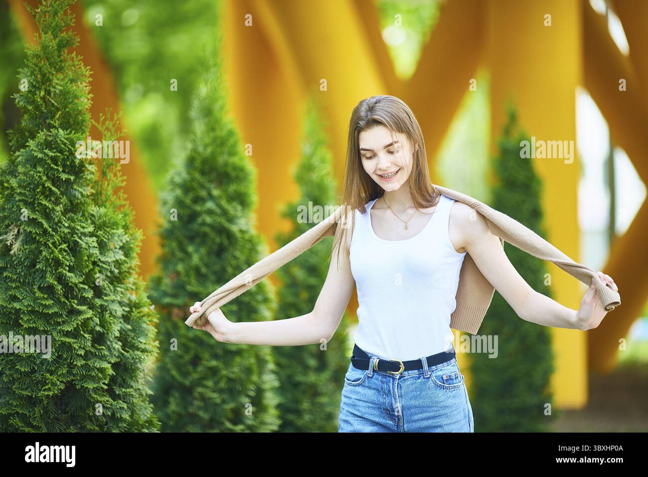 Junge Teenager-Frau, die an einem Sommertag in Jeans und Pullover die Straße entlang läuft. Das Konzept der Jugendmode. Urbaner Lebensstil Stockfoto