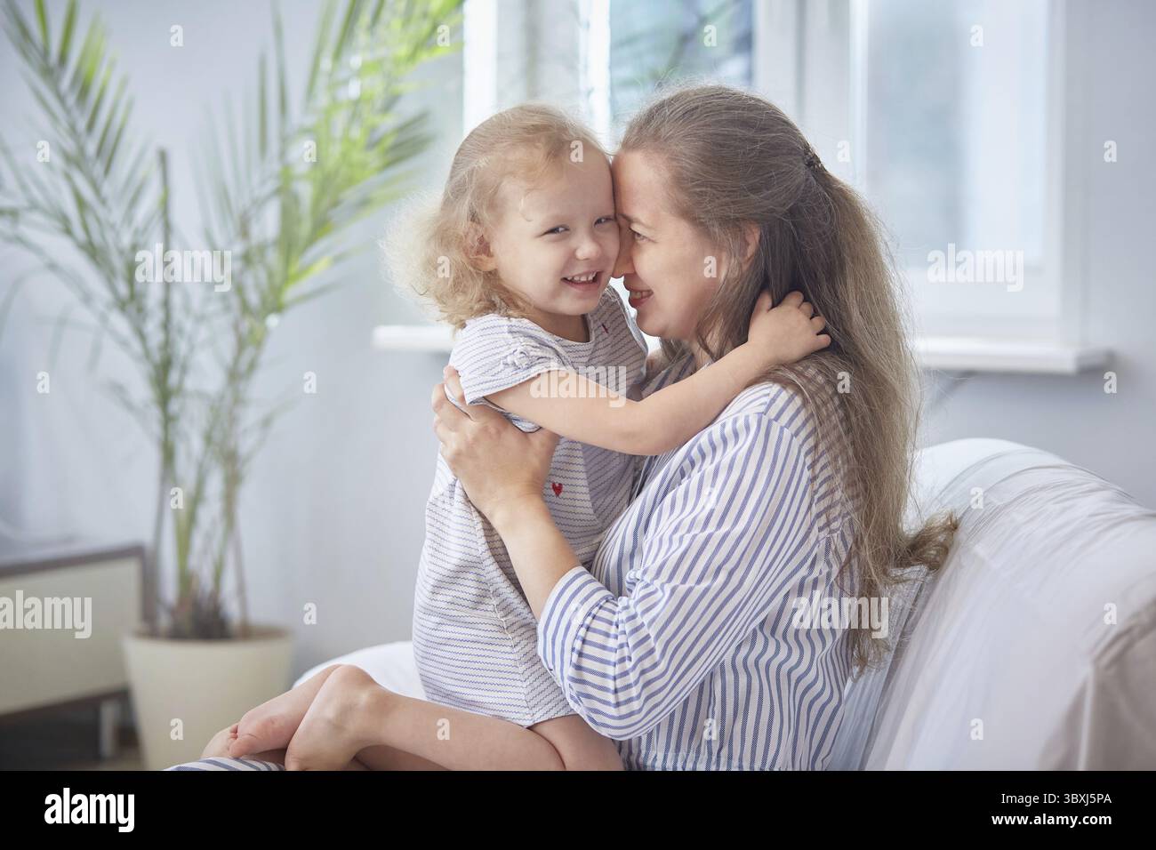Glücklicher Muttertag. Mom und Tochter lächeln und umarmen sich zu Hause auf dem Sofa in einem hellen Zimmer. Das Konzept des Familienglücks mit Kindern. Familie Stockfoto