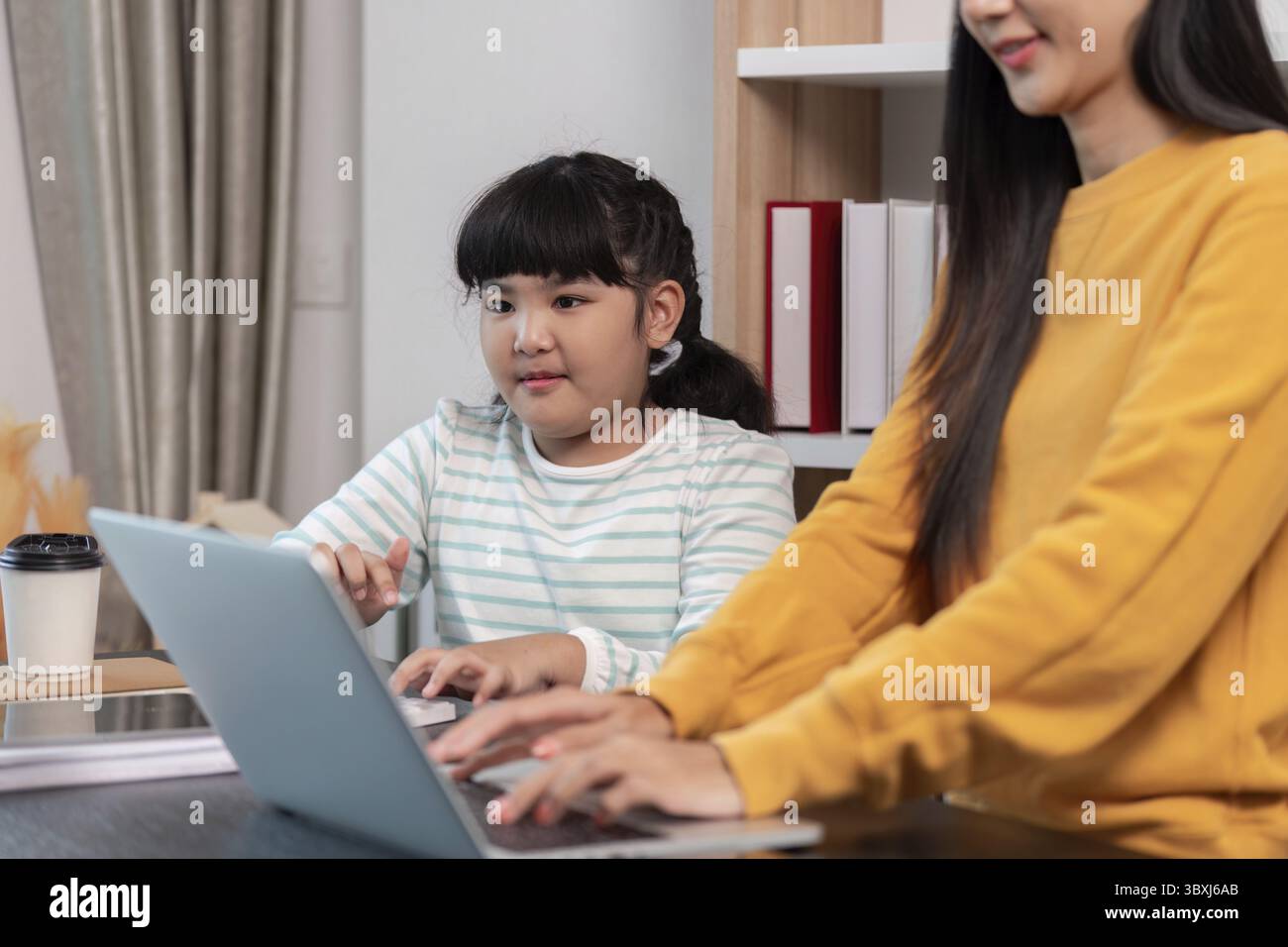 Mutter und Tochter sitzen zusammen und nehmen an Aktivitäten auf einem gemeinsamen Laptop Teil, um die Verbindung und das gemeinsame Lernerlebnis hervorzuheben Stockfoto