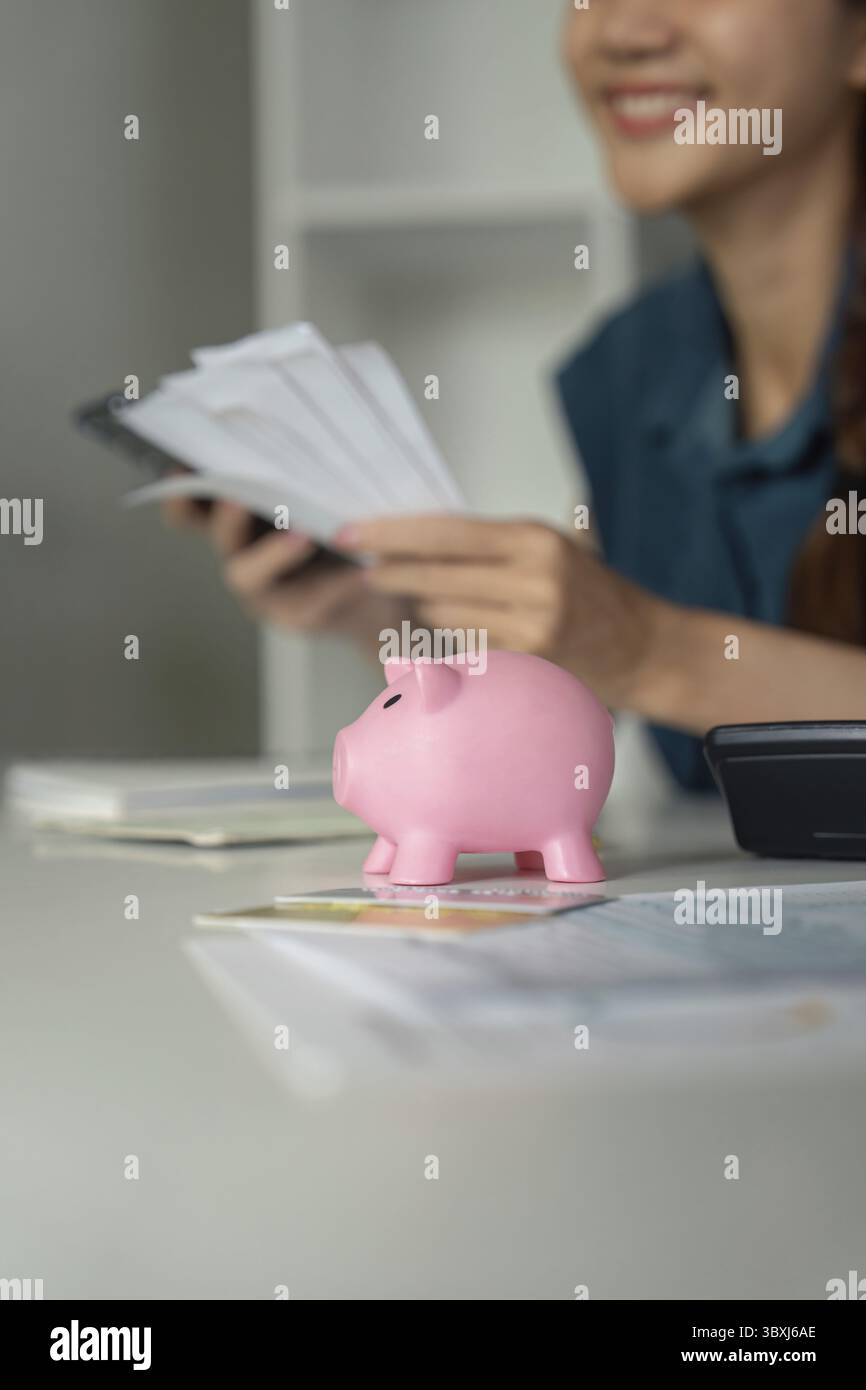 Eine Person lächelt, während sie die Belege und ihre Ersparnisse überprüft und mit einer Sparkasse über ihren finanziellen Fortschritt und zukünftige Ziele nachdenkt Stockfoto