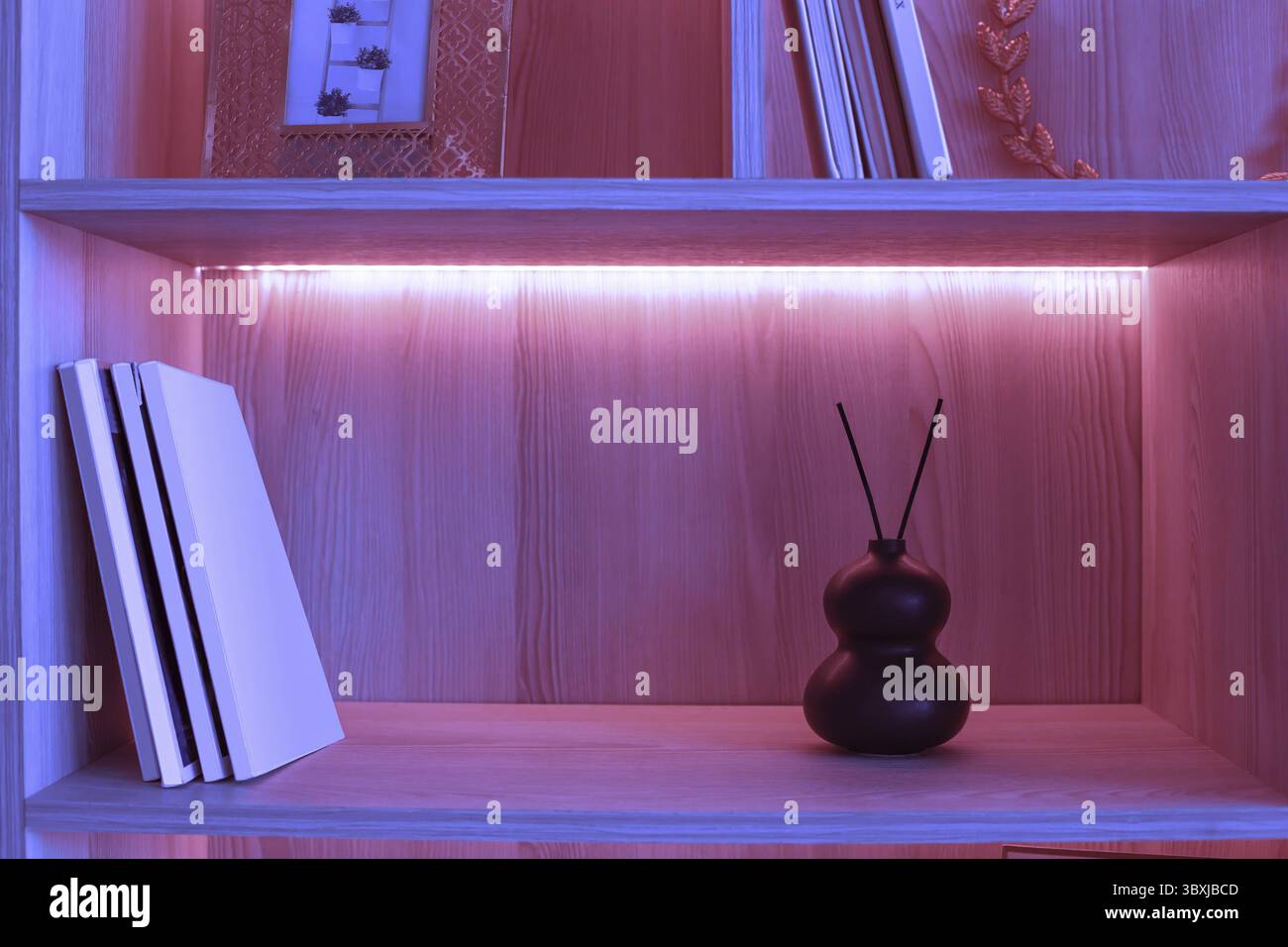 Auf einem Regal mit rosafarbener Neonbeleuchtung befindet sich eine kleine schwarze Keramikvase mit zwei Aromastöcken. Kopierbereich Stockfoto