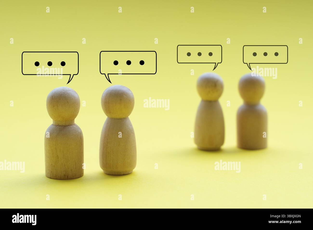 Holzfiguren, die miteinander sprechen, auf gelbem Hintergrund, die Netzwerkarbeit darstellen oder geschäftliche Geschäfte betreiben Stockfoto