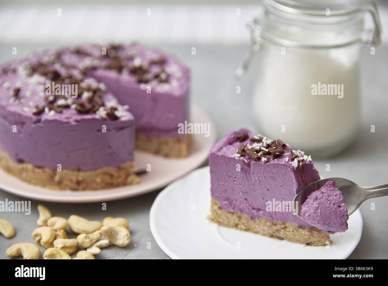 Veganer roher Blaubeerkuchen. Die Hand mit dem Löffel bricht ein Stück Kuchen ab. Die Anwesenheit einer Person ohne Gesicht Stockfoto