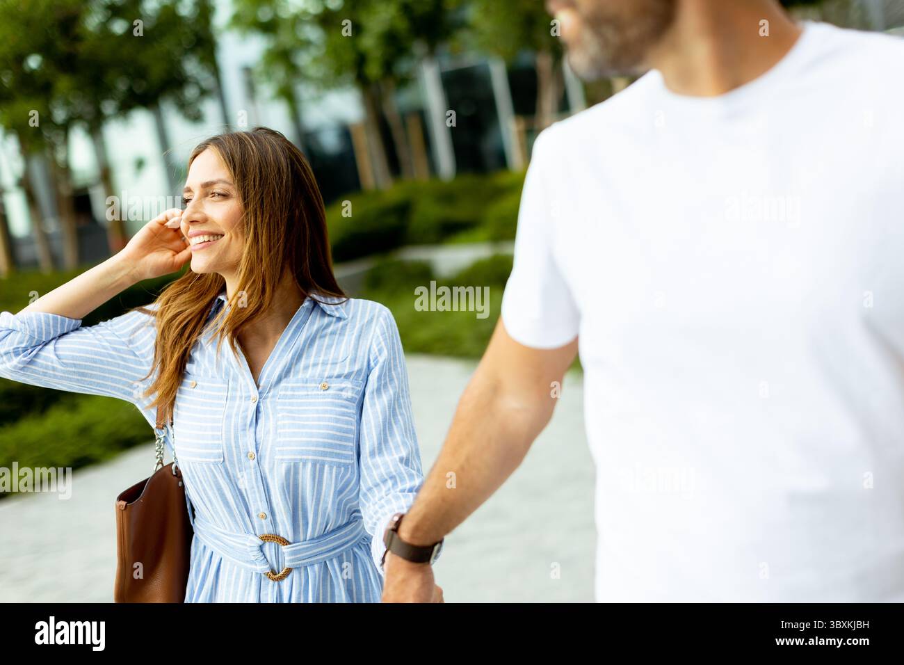 Zwei Freunde genießen die Wärme eines sonnigen Tages und gehen Hand in Hand durch einen üppigen Stadtpark voller Grün und Lachen. Stockfoto