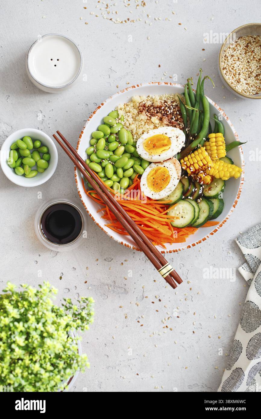 Gesunder Salat mit Couscous, Karotten, Gurken, grünen Bohnen, Sojabohnen, Mais und ein Ei auf grauem Betongrund. Lebensmittel und Gesundheit. Buddha-Schale Sal Stockfoto