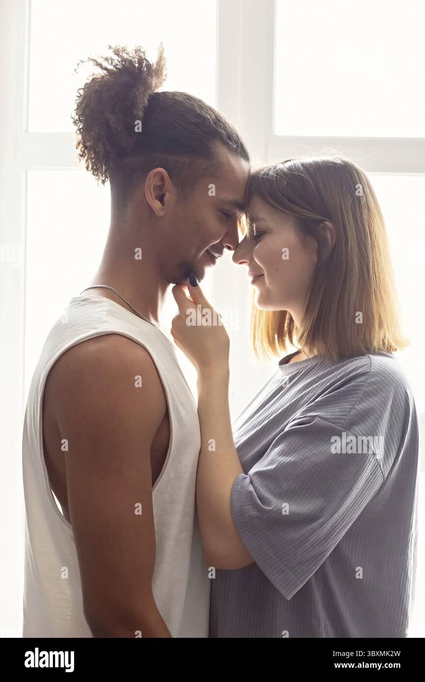 Porträt eines multirassischen Paares, Freund und Freundin von Angesicht zu Angesicht, stehen in der Nähe des Fensters Stockfoto