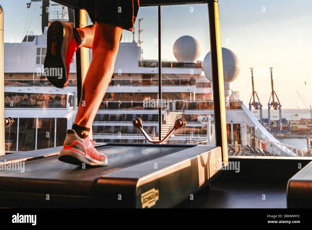 Die Beine eines Mannes, der auf dem Laufband im Health Club neben dem großen Fenster läuft. Konzept für Training, Fitness und gesunden Lebensstil. Selektiver Fokus Stockfoto