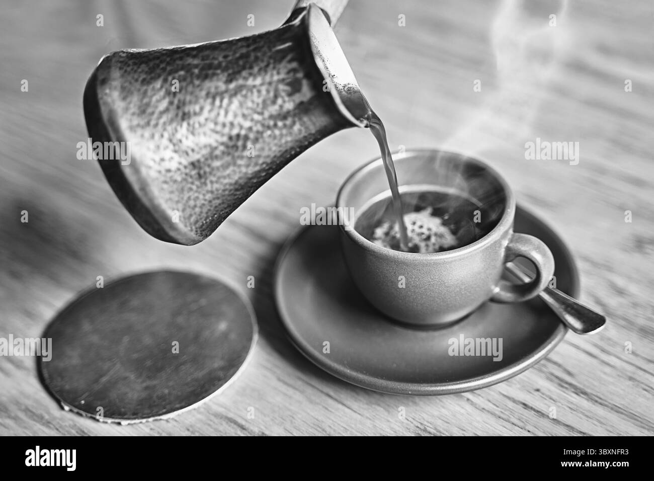 Heißer Kaffee mit Dampf im orientalischen türkischen Stil, serviert in Cezve, eine kleine, langstielige Kanne mit einer ausgießenden Lippe und Tasse auf einem Holztisch in Schwarz und wh Stockfoto