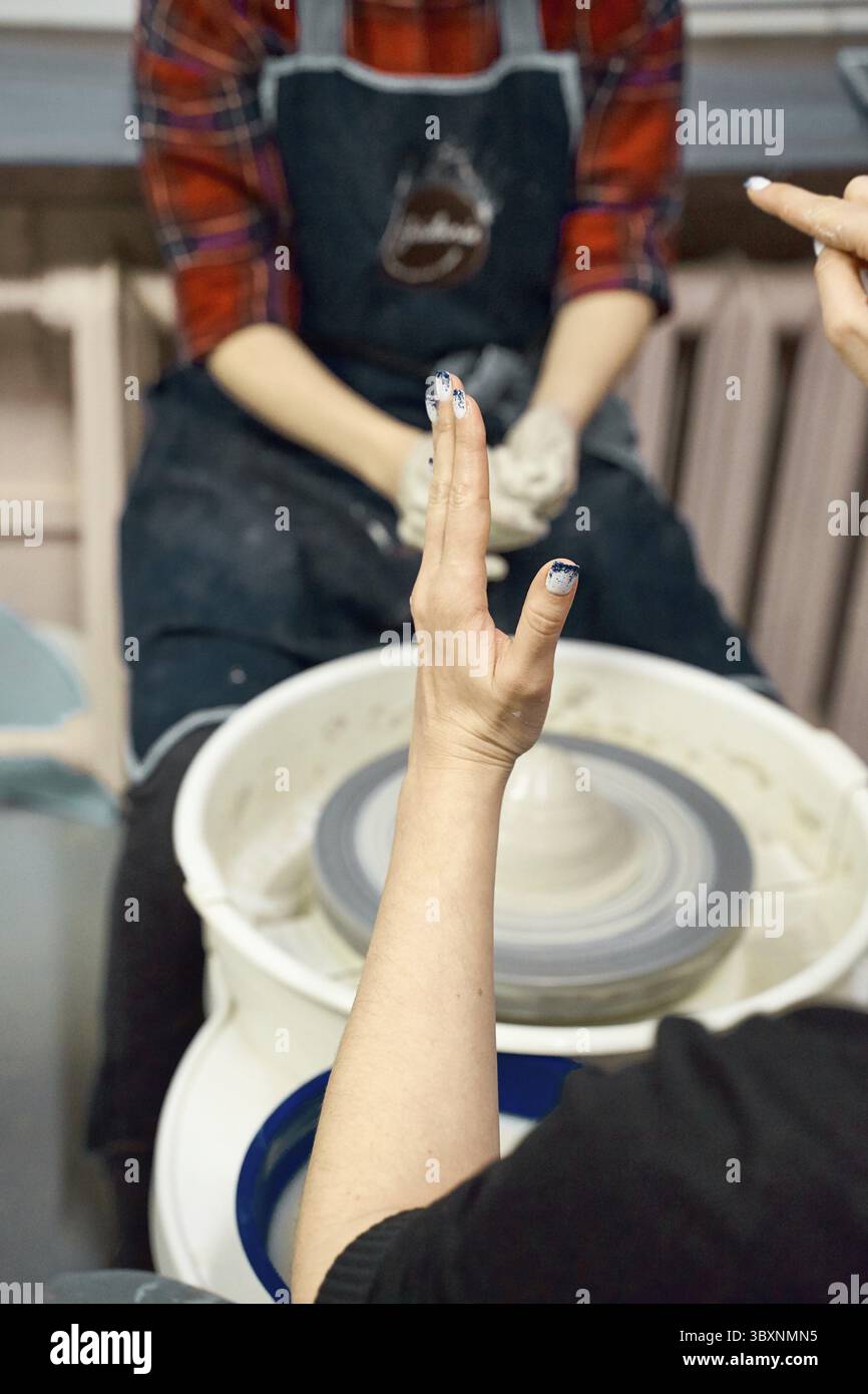 Frau lehrt Töpferei auf Töpferscheibe, Meisterklasse, Werkstatt. Kreatives Hobby-Konzept. Verdienen Sie mehr Geld, Side Hustle, vertikal Stockfoto