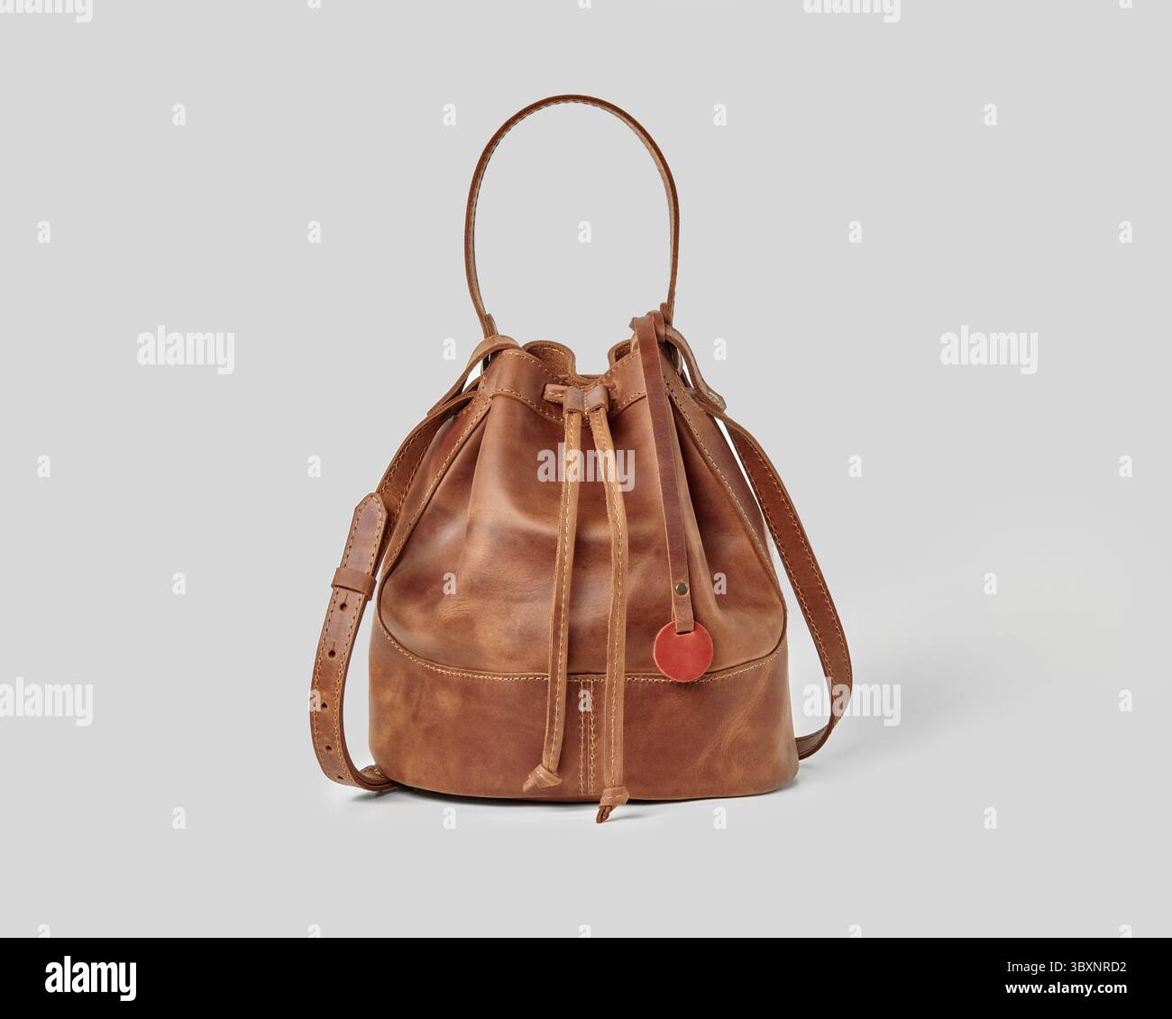 Elegante, elegante Etui aus braunem Leder mit verstellbaren Kordelzügen und Schultergurt, isoliert auf grauem Hintergrund Stockfoto