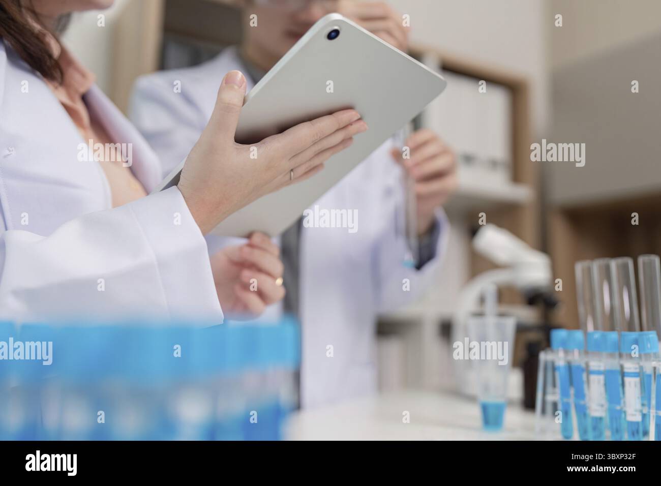 Ein Forscher verwendet ein Tablet-Gerät, um Daten während chemischer Experimente zu sammeln, wobei er sich auf digitale Aufzeichnungen und Genauigkeit konzentriert Stockfoto