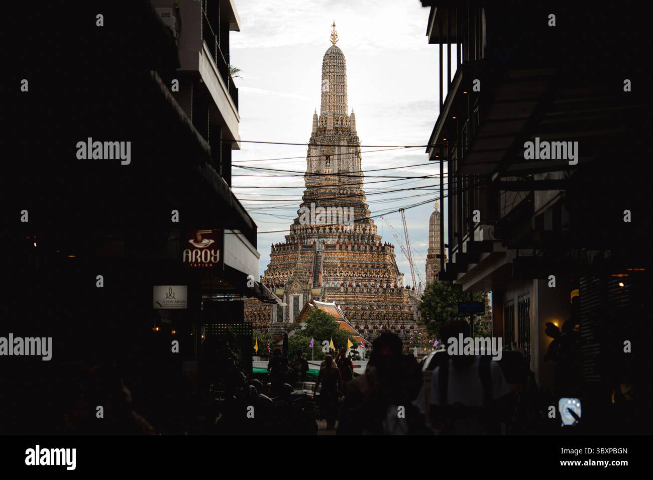 18. Juli 2025, Bangkok, Thailand: Die zentrale Pagode des Wat Arun erhebt sich zwischen schmalen Gebäuden entlang einer Flussallee in Bangkok. Auch bekannt als der Tempel der Dämmerung, ist der Ort ein prominentes Symbol des thailändischen Erbes und der Architektur. Die Stätte wurde offiziell in die Liste der UNESCO-Weltkulturerbestätten aufgenommen, was einen wichtigen Schritt hin zur vollständigen Anerkennung als Weltkulturerbe darstellt. Diese Aufnahme wurde von der UNESCO im April 2025 bestätigt, und der formelle Prozess für eine mögliche Inschrift des Weltkulturerbes läuft derzeit. (Credit Image: © ploy Phutpheng/SOPA images via ZUMA Press Wire) EDI Stockfoto