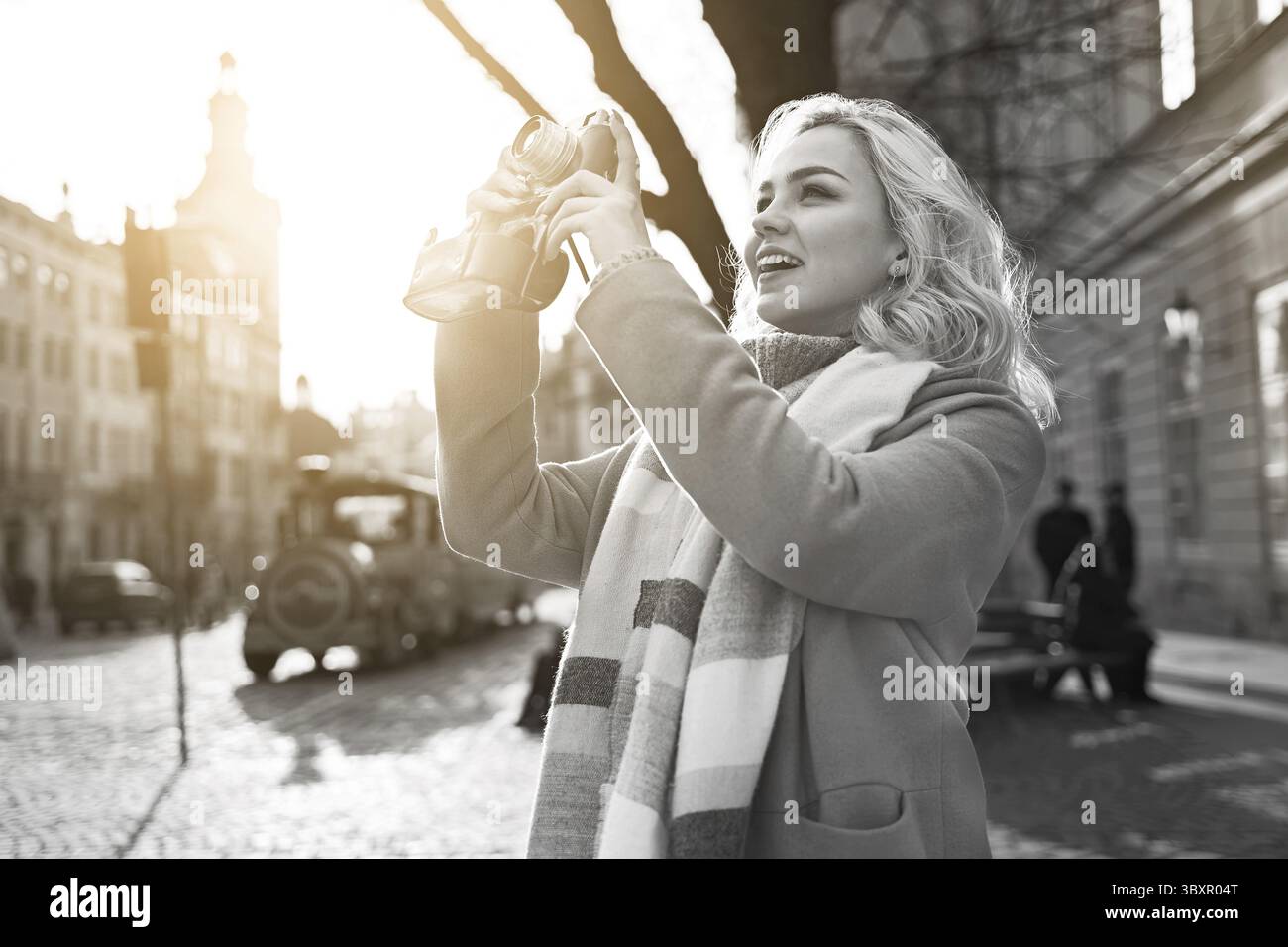 Junge schöne, fröhliche blonde Frau, die an einem sonnigen Tag auf dem Rynok-Platz in Lemberg, Ukraine, Fotos mit ihrer Vintage-Filmkamera macht Stockfoto