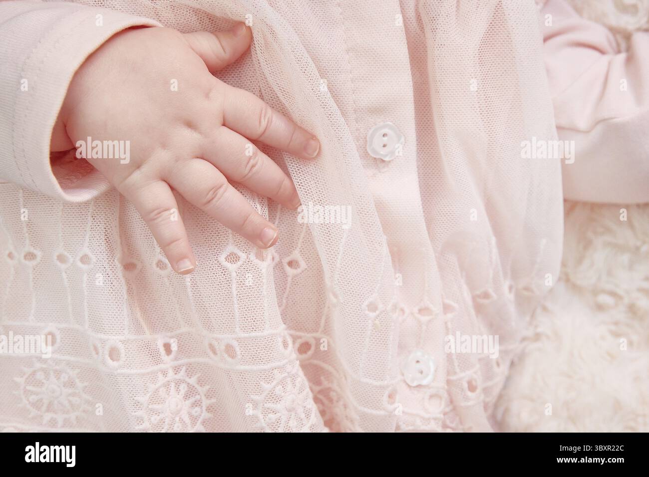 Nahaufnahme der Hand eines neugeborenen Mädchens in einem rosa Kleid mit Spitze und Stickerei. Postkarte ist ein Mädchen. Copyspace Stockfoto