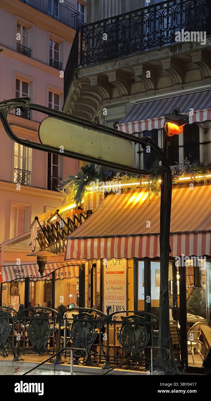 Abendliche Szene eines einladenden Pariser Cafés mit rot-weiß gestreifter Markise und dezenter Beleuchtung. Das warme Ambiente schafft eine gemütliche Atmosphäre für Gäste Stockfoto