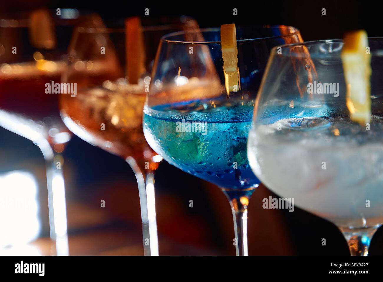 Eine bunte Auswahl an Cocktails in eleganten Gläsern mit leuchtenden Blau- und Orangetönen, garniert mit Zitrusschalen, perfekt für festliche Feiern Stockfoto