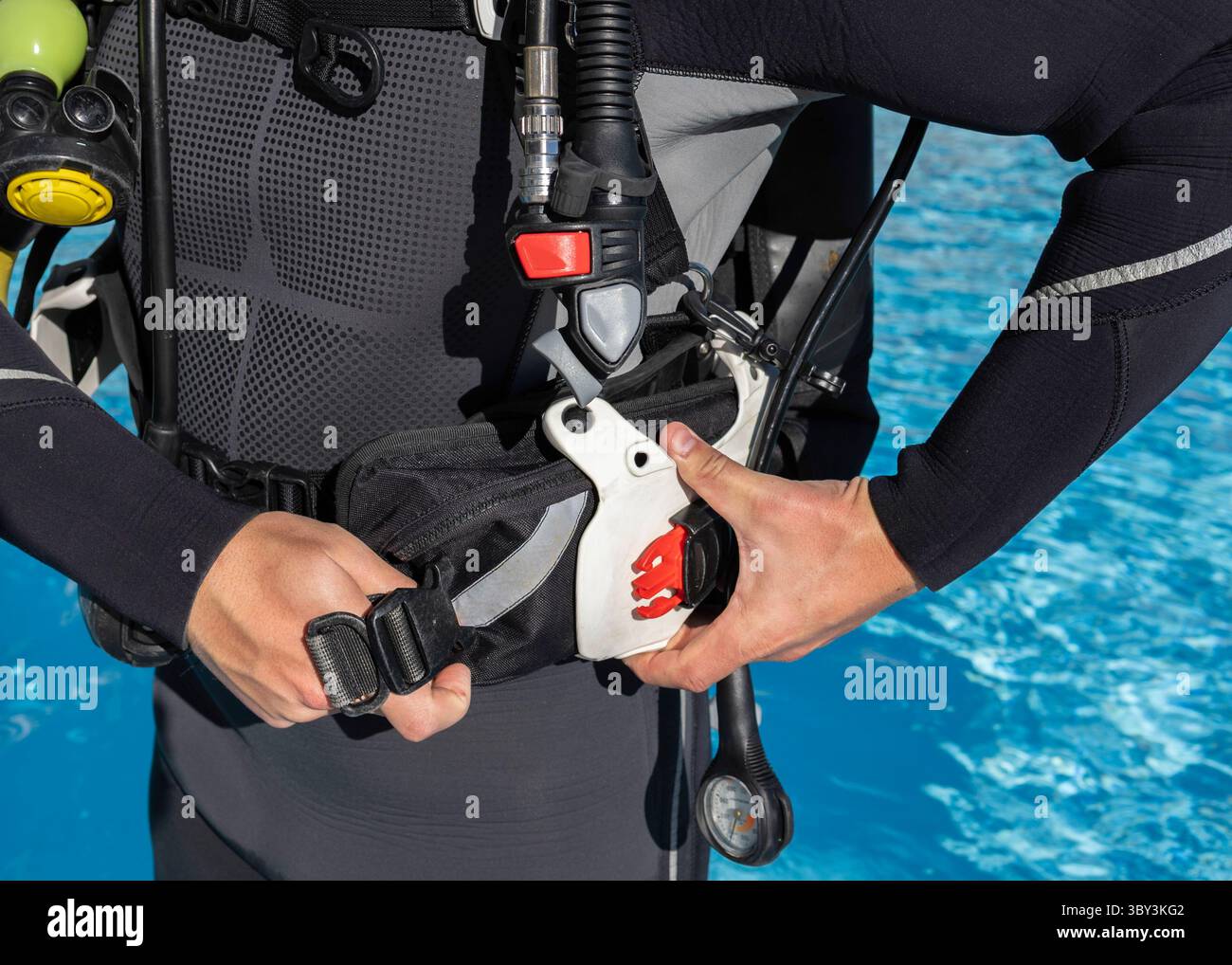 Nahaufnahme eines Tauchers, der seine Gewichtstasche in seine BCD-Tasche neben einem Pool steckte. Stockfoto