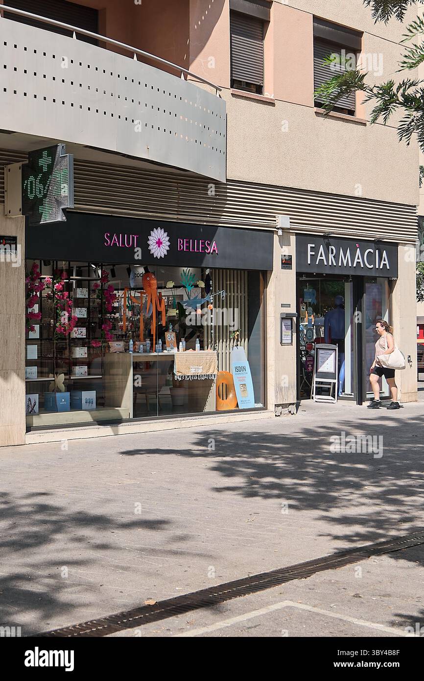 Viladecans.Barcelona - 19. Juli 2025: Blick auf mehrere Gewerbebetriebe, darunter eine Clinic de La Riera und eine Farmàcia, mit einer Frau in Sport Stockfoto