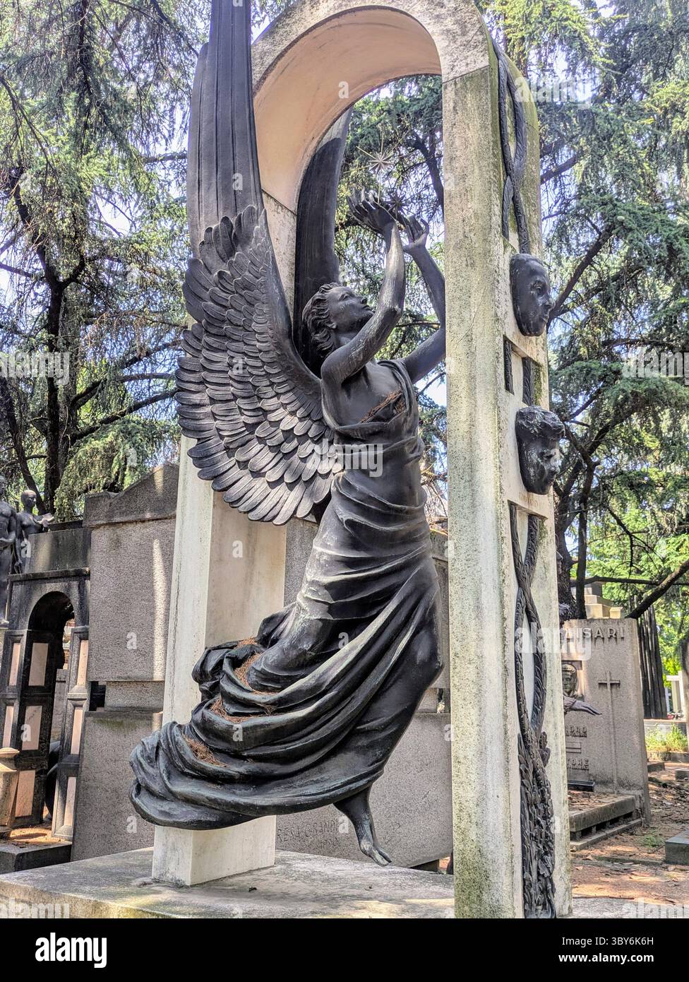 Engelsstatue mit Flügeln unter Steinbogen, umgeben von Bäumen auf dem Friedhof Stockfoto