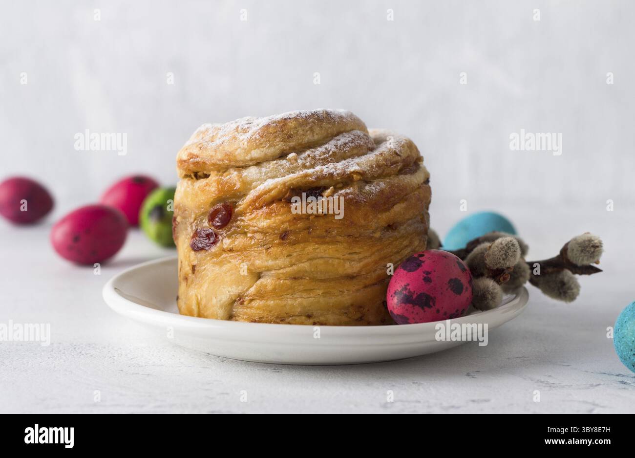 Essen, Osterkuchen Kraffin mit Nüssen und getrockneten Früchten, bestreut mit Puderzucker, dekoriert mit einem bemalten Ei und Weidenzweigen auf einem hellblauen Stockfoto
