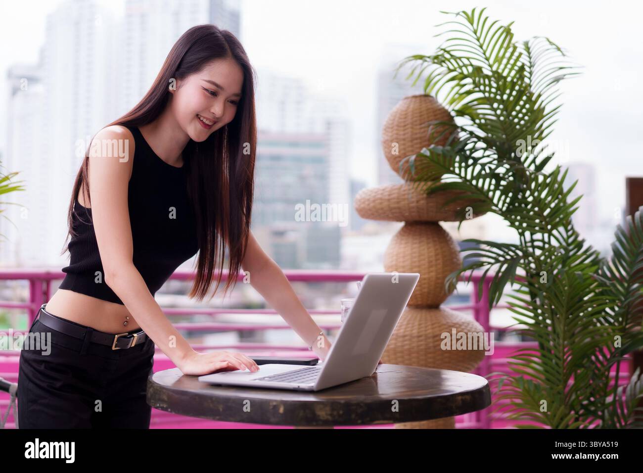 Selbstbewusste, moderne asiatische professionelle Erwachsene Frau lächelt, die im Freien mit Technologie in der geschäftigen Stadtumgebung arbeitet Stockfoto