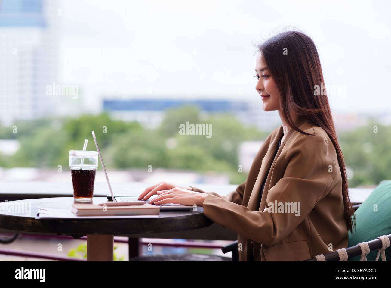 Selbstbewusste asiatische Frau, die im Freien an einem Laptop arbeitet Sie konzentriert sich auf ihre Geschäftsaufgaben und genießt einen flexiblen, modernen Arbeitsstil Stockfoto