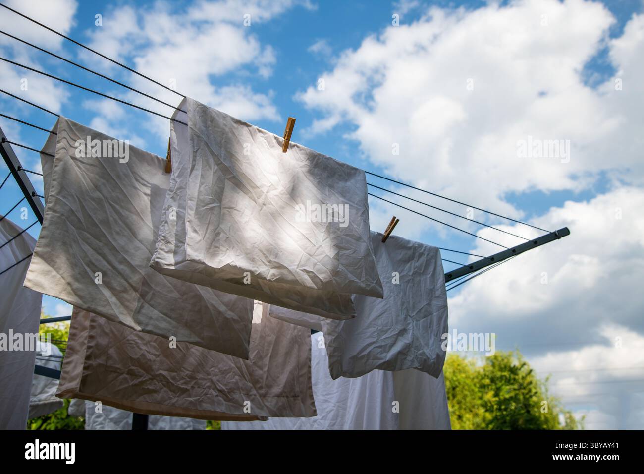 Wäsche hängt an einer rotierenden Wäscheleine vor einem hellblauen Himmel mit verstreuten Wolken und fängt einen frischen, luftigen Tag und den Alltag im Haushalt ein. Stockfoto