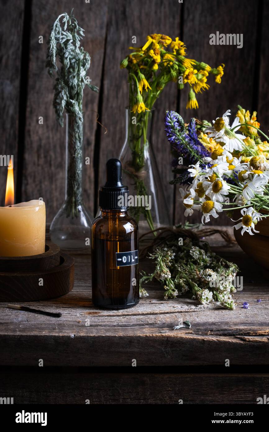 Ätherisches Öl in Glasflasche mit Wildblumen und Kerzen Stockfoto