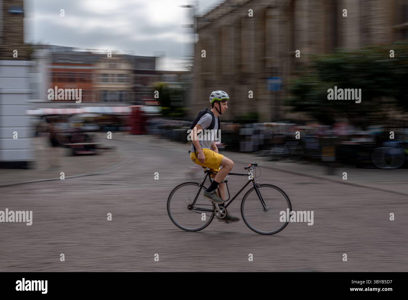 Cambridge, England, Großbritannien - 13. Juli 2025: Schwenkfoto eines Radfahrers, der freihändig durch die sonnige Stadtstraße auf dem Campus fährt und nach rechts blickt Stockfoto