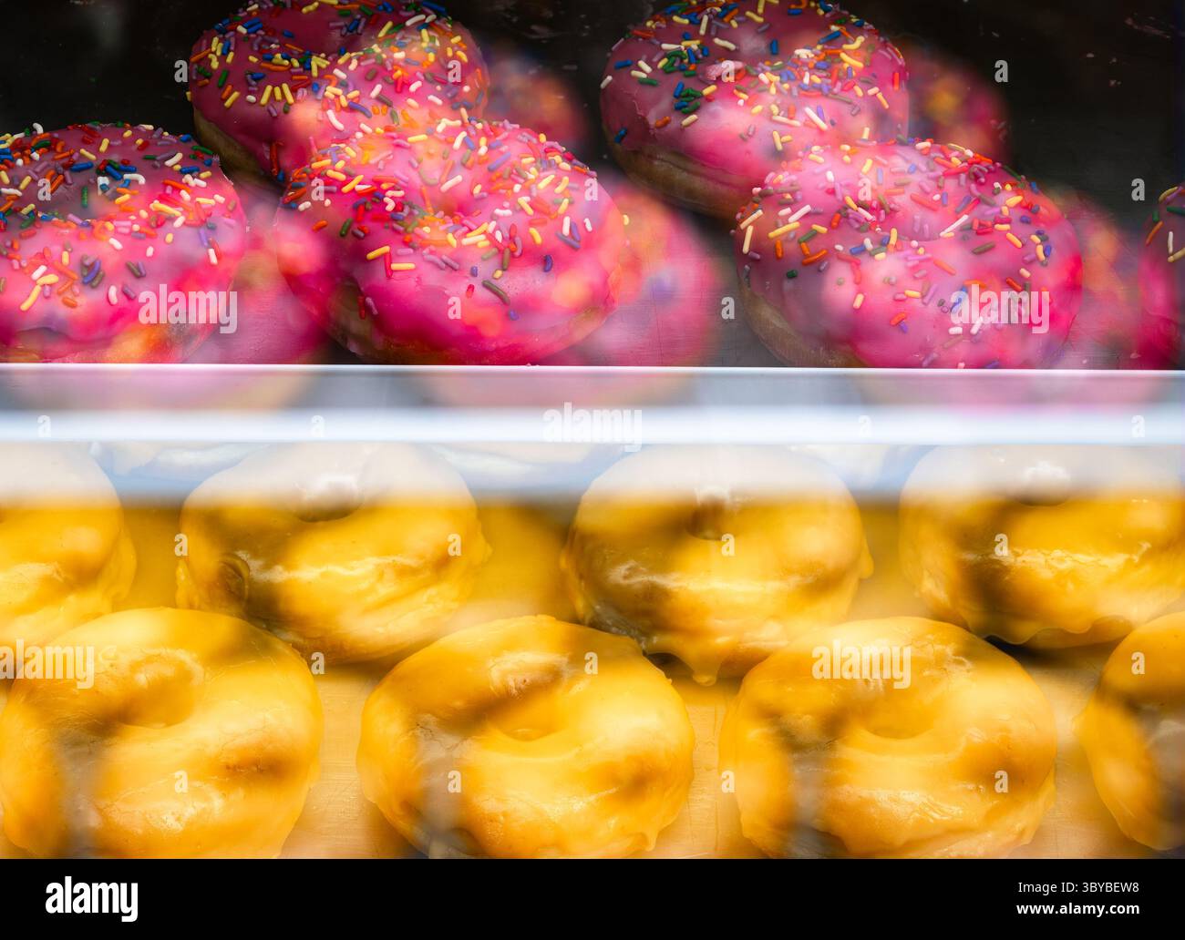 Eine Vitrine mit rosafarbenen, mattierten Donuts mit Streuseln und glasierten Donuts. Stockfoto