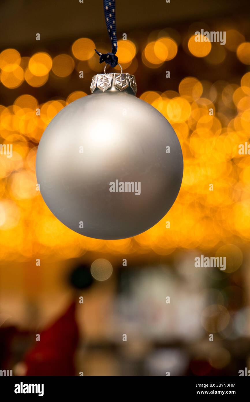 Silberne Weihnachtskugel hängt mit verschwommenen Weihnachtslichtern im Hintergrund Stockfoto