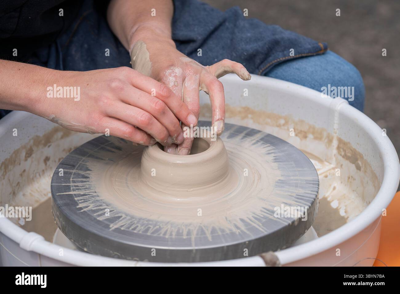 Nahaufnahme von weiblichen Töpferhänden, die eine Schüssel machen. Die Frau schlang die Hände um nassen Ton auf einem Töpferrad. Frau, die Keramik in der Töpferwerkstatt herstellt. Stockfoto