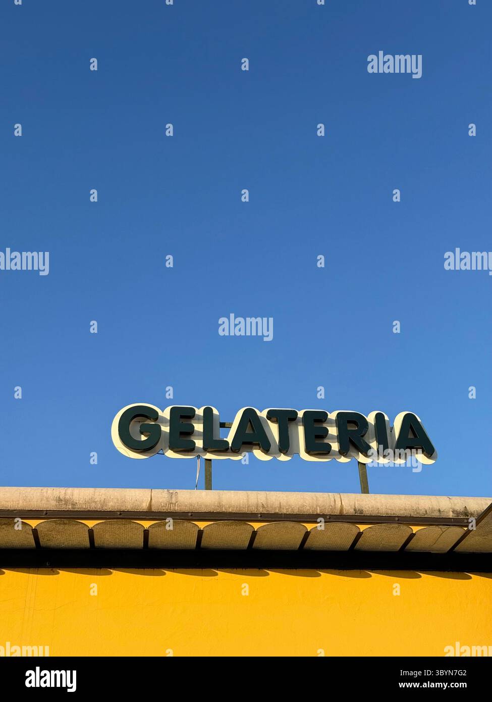 Eiscreme (Gelateria) Ladenschild auf gelbem Dach im Kontrast zum leuchtend blauen Himmel. Bardolino am Gardasee, Italien Stockfoto