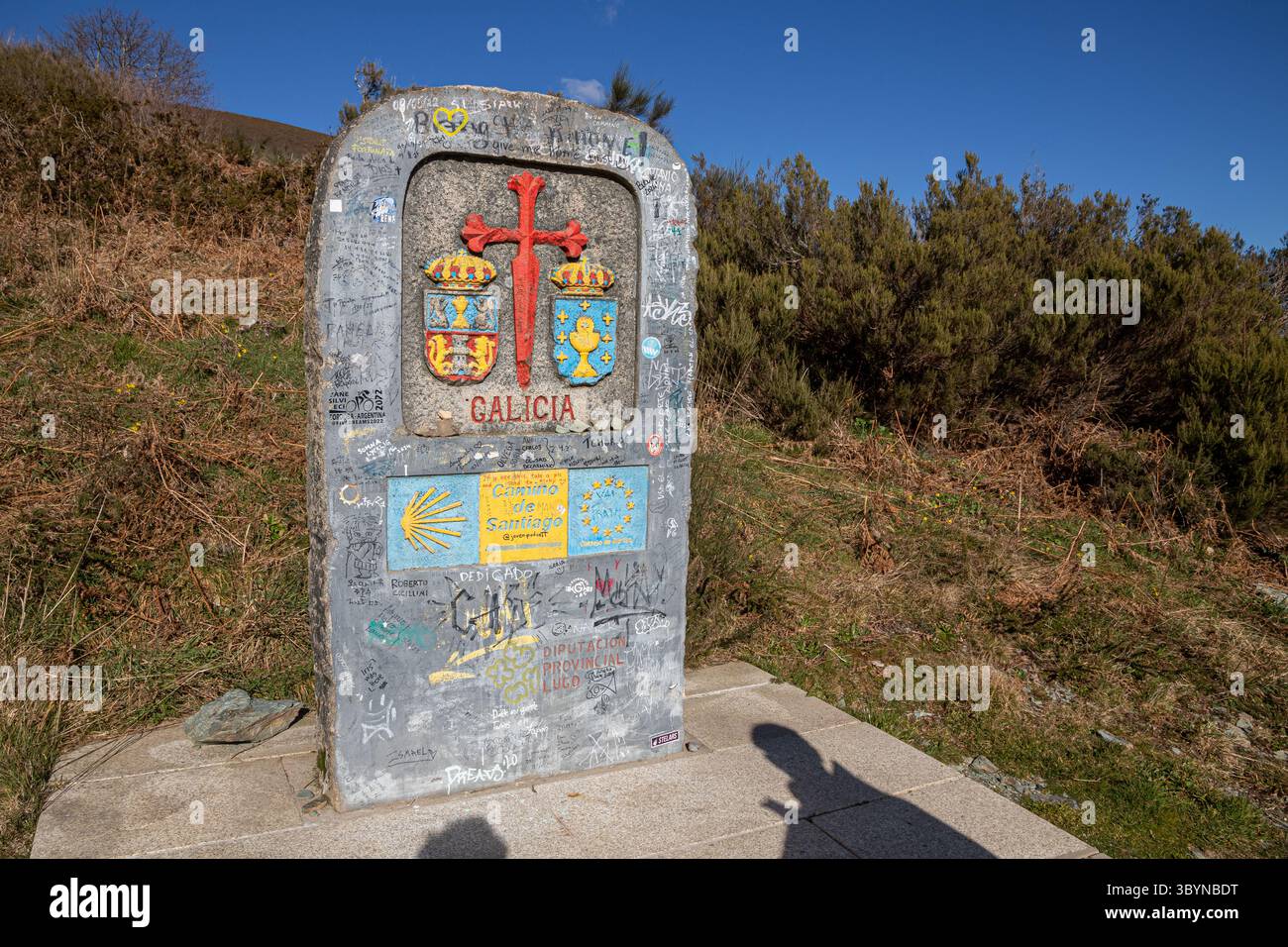 O Cebreiro, Spanien. Monolith markiert die Grenze zwischen Castilla y Leon und Galicien mit rotem Santiago-Kreuz, Graffiti- und Pilgersignaturen, Jakobsmuscheln Stockfoto