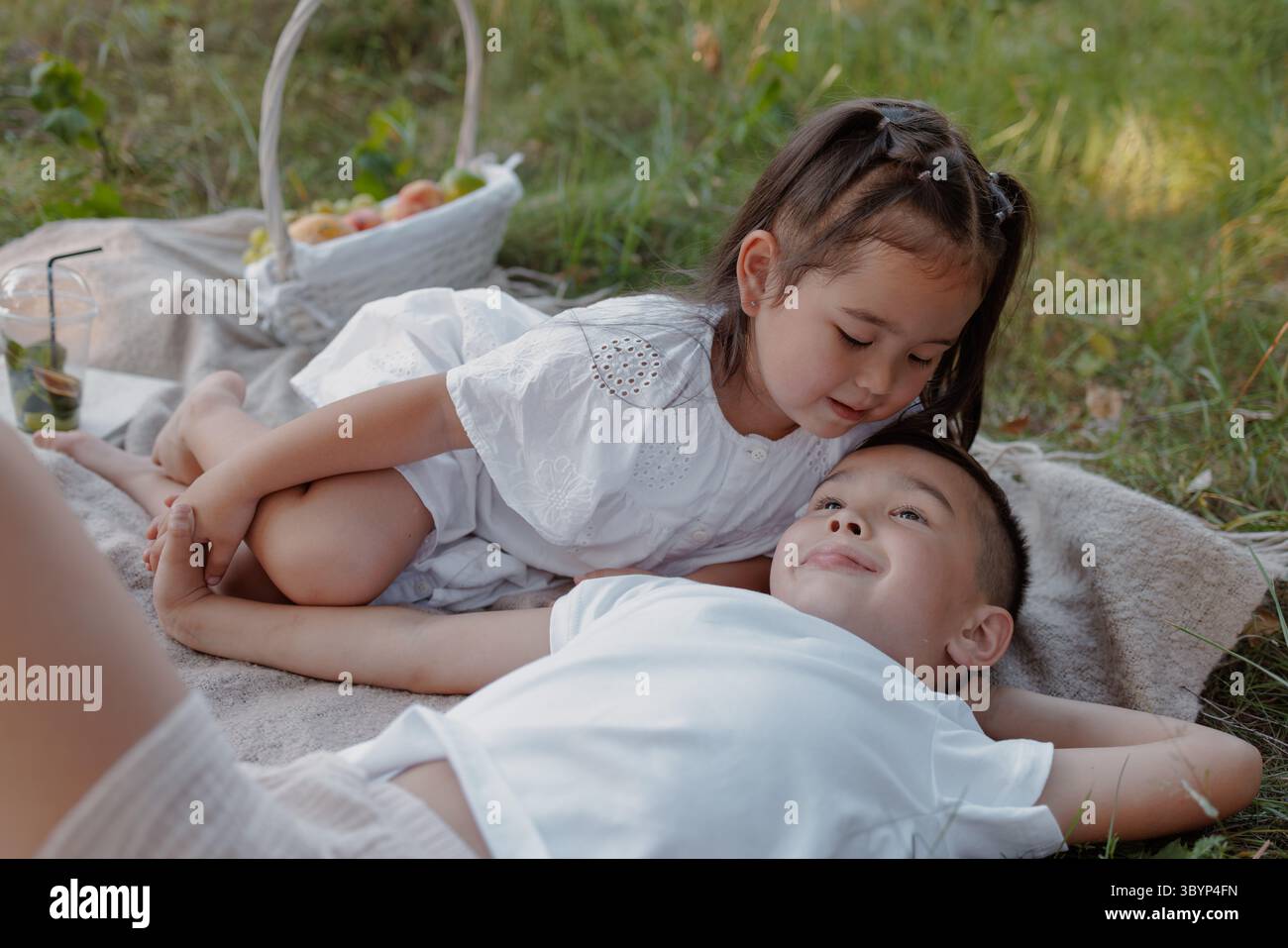 Zwei Kinder entspannen sich auf einer Picknickdecke im Gras und teilen sich einen süßen Geschwistermoment während eines Sommertages mit der Familie Stockfoto